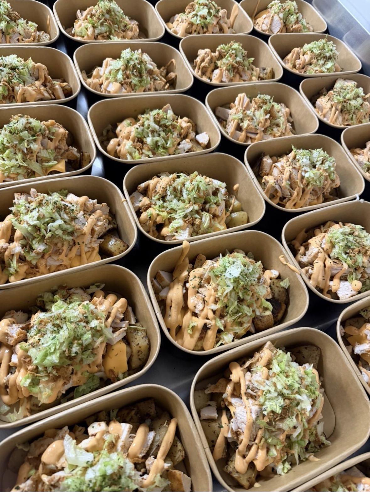 Chicken and roast potato boxes topped with shredded lettuce and a creamy sauce drizzle